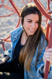 Thoughtful young woman smiling while sitting amidst rope at playground