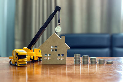 Close-up of model home with toy trucks and coins on table at home