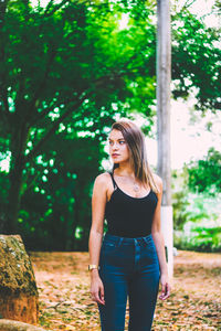 Teenage girl looking away while standing against trees