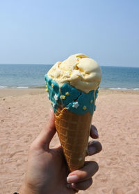 Midsection of ice cream cone on beach against sky