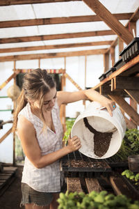 Female farmer pouring mud in seedling tray at greenhouse