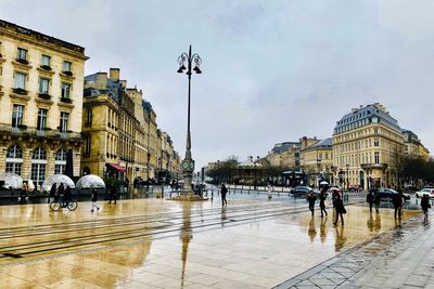 People walking on wet street against buildings during rainy season