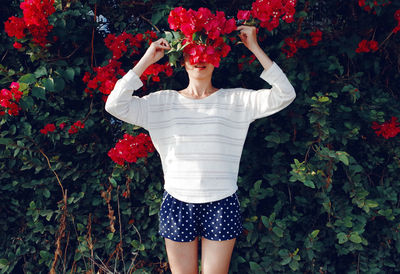 Young woman holding flowers while standing by plants in park