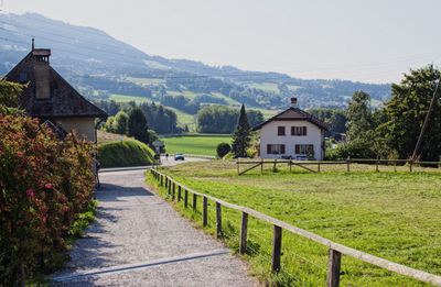 Road leading towards houses by mountain against sky