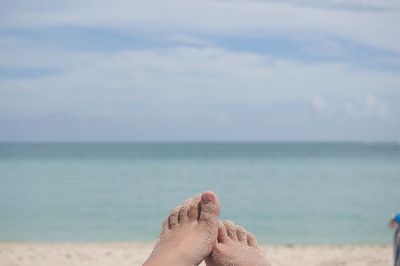 Close-up of human feet on beach by sea against sky