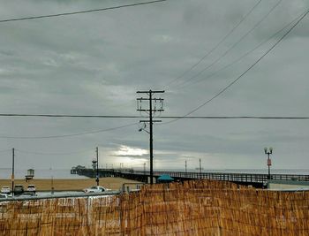 Power lines on field against cloudy sky