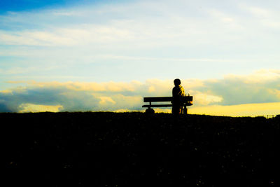 Rear view of man standing on field against sky during sunset