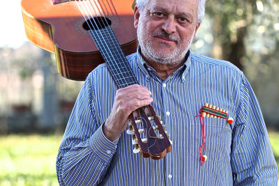 Portrait of senior man holding guitar while standing outdoors