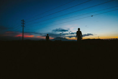 Silhouette people on landscape against sky during sunset