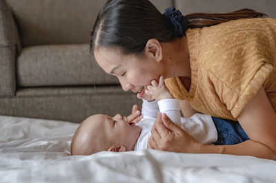 Side view of smiling mother playing with cute son lying on bed at home