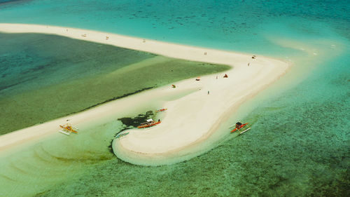 Tropical white island and sandy beach with tourists surrounded by coral reef and blue sea