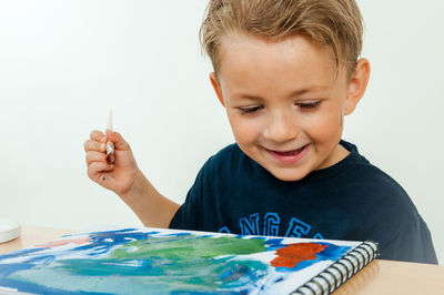 Cute happy boy painting on book against white background
