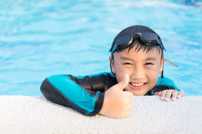 Portrait of smiling boy gesturing thumbs up in swimming pool