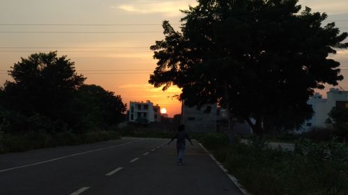 Silhouette person on road by trees against sky during sunset