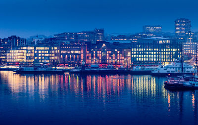 Illuminated buildings by river against sky at dusk