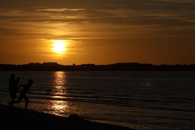 Silhouette people on beach against sky during sunset