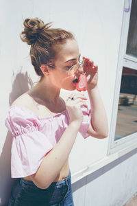 Young woman licking flavored ice against wall
