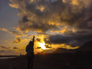 Rear view of silhouette woman standing at beach against sky during sunset