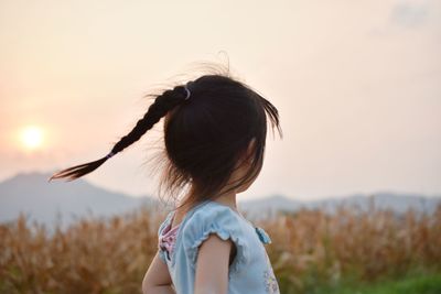 Side view of girl shaking head against sky during sunset