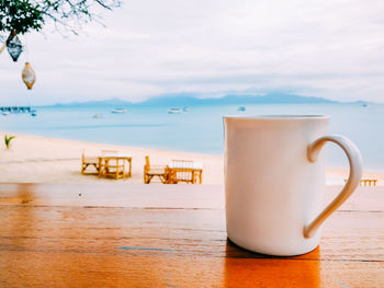 Coffee cup on table by sea against sky