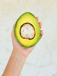 Cropped image of hand holding avocado against white wall