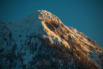 Low angle view of snowcapped mountains against clear blue sky