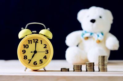 Stacked coins and alarm clock with teddy bear on table