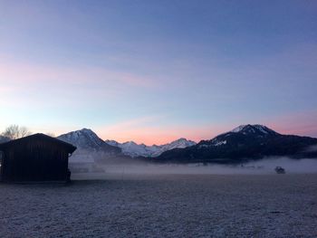 Silhouette house against snowcapped mountains at sunset