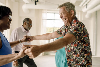 Cheerful senior man holding hands of woman while dancing in class