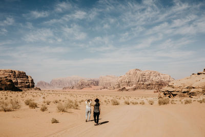 Rear view of friends walking at desert against sky during sunny day