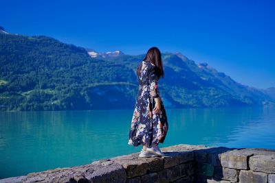 Rear view of woman standing by lake against mountains