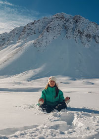 Full length of woman sitting on snowcapped mountain in lotto position 