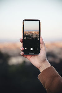 Close-up of hand holding smart phone against sky