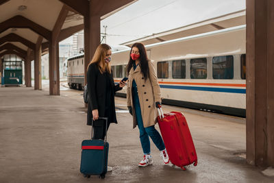 Full length of women wearing mask holding suitcase standing on railroad platform