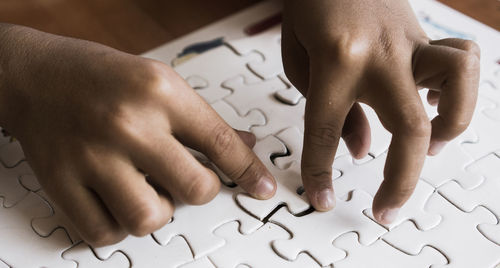 Cropped hands of child solving jigsaw puzzle on table
