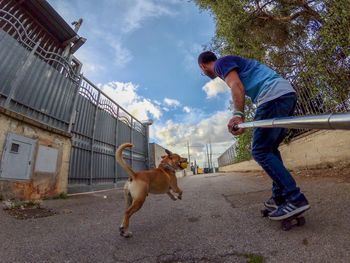 Man holding monopod by skateboarding by dog on footpath