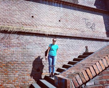 Full length portrait of woman standing on steps against building during sunny day