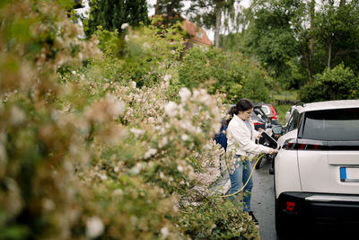 Woman charging electric car while standing by plants