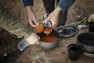 Hands putting food from can into pot