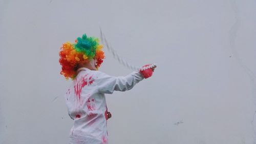 Low angle view of boy wearing costume swinging chain standing against wall