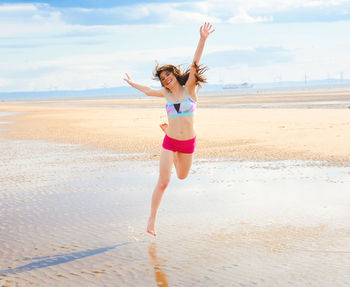 Full length of young woman with arms raised on beach