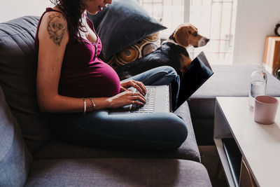 Midsection of woman with dog sitting on sofa at home