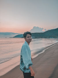 Full length of man standing on beach against sky during sunset