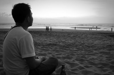 Rear view of man sitting on beach against sky