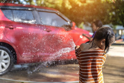 Rear view of girl washing car outdoors