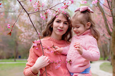 Portrait of mother and daughter in the park with blooming pink sakura