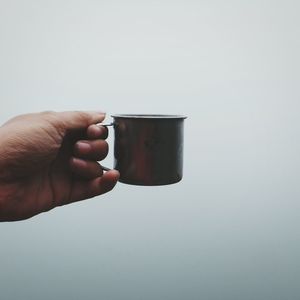 Close-up of hand holding coffee cup against white background