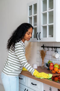 African-american woman occupied with household duties in kitchen. wearing yellow rubber gloves