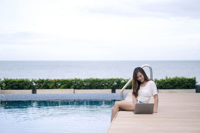 Woman sitting in swimming pool against sea