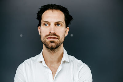 Thoughtful mid adult man looking away while standing against wall